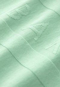 Mátově zelená látka s texturovanou výšivkou, obsahující písmena, hladké pletené části a kontrastní žebrované horizontální pruhy.