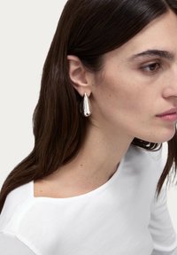 Silver teardrop earrings with a reflective surface, worn by a model with long dark hair, complementing a white top.