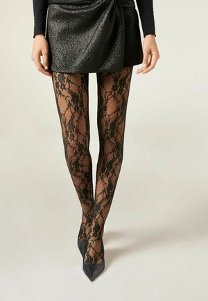 Sorte blonderet strømpebukser med blomstermønster og små ædelsten, parret med en struktureret sort mini-nederdel og spidse sorte hæle.