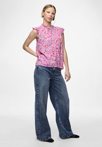 Blusa senza maniche rosa con un motivo floreale, spalle arricciate e dettaglio a chiave, abbinata a jeans in denim blu a gamba larga.