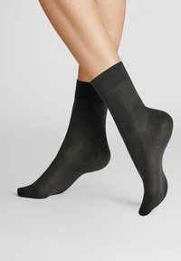 Schwarze Knöchelsocken aus einem glatten, transparenten Stoff. Mit einem engen, elastischen Bund und einer passgenauen Form, die sich an den Fuß anpasst.