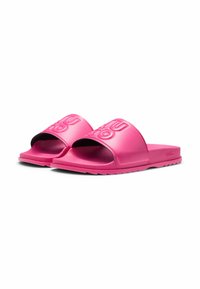 Pink slide sandals made of smooth rubber, featuring a wide strap with embossed logo, textured insole, and a flat sole.