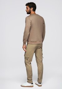 Beige mikina s kulatým výstřihem, slim fit. Slučena s béžovými cargo kalhotami s kapsami na zip a klopou. Bílé tenisky s hnědými podrážkami.