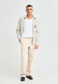 Striped, light green and white shirt over a white t-shirt, paired with beige pants and black shoes; casual fit, visible pocket detail.
