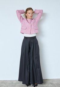 Rausvo tweedo švarkas su auksiniais mygtukais, priekinių kišenių, derinamas su juodomis plačiomis kelnėmis su aukštu liemeniu. Lygios tekstūros ir struktūruoto kirpimo.