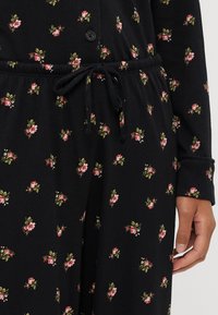 Set de pijama negru cu modele florale mici în nuanțe de roz și verde, având un front cu nasturi și o talie cu șnur pentru ajustare.
