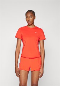 Fluoreszkáló narancssárga sportpóló és rövidnadrág, könnyű anyagból készült, kerek nyakkivágással és fehér Nike logóval.