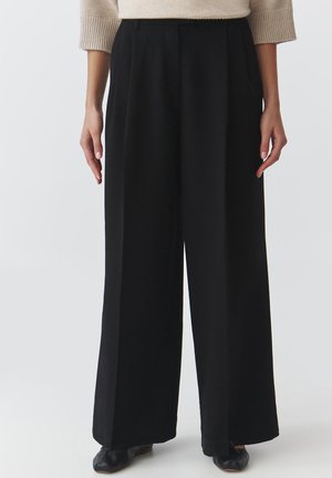 Zwarte broek met wijde pijpen en een hoge taille, voorzien van voorplooien en een gladde stofstructuur, gecombineerd met zwarte schoeisel.