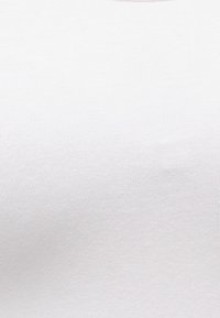 Λευκό ύφασμα με ριμπ υφή σε στενή λήψη με λεπτή υφή και απαλά σκιασμένα πτυχώματα, που δείχνει το λεπτό πλεκτό σχέδιο και την απαλότητα της επιφάνειας του υλικού.