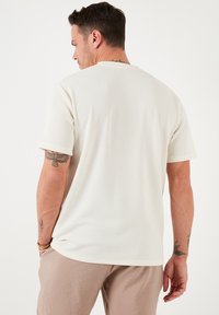 Hvid ribbet t-shirt med korte ærmer og rund halsudskæring. Viser et struktureret stof og afslappet pasform, parret med beige bukser.