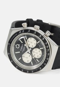 Montre chronographe avec un cadran noir, un boîtier en acier inoxydable argenté, trois sous-cadrans et un bracelet noir. Comprend une échelle tachymétrique sur la lunette.
