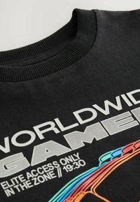 Czarna bluza z ribbowanym dekoltem, odważnym białym napisem "WORLDWIDE GAMER" oraz kolorowymi akcentami graficznymi w czerwonym, niebieskim i żółtym.