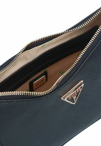 Borsa sintetica nera con texture, zip dorata e logo triangolare brandizzato. L'interno presenta una fodera beige con dettagli stampati verdi.