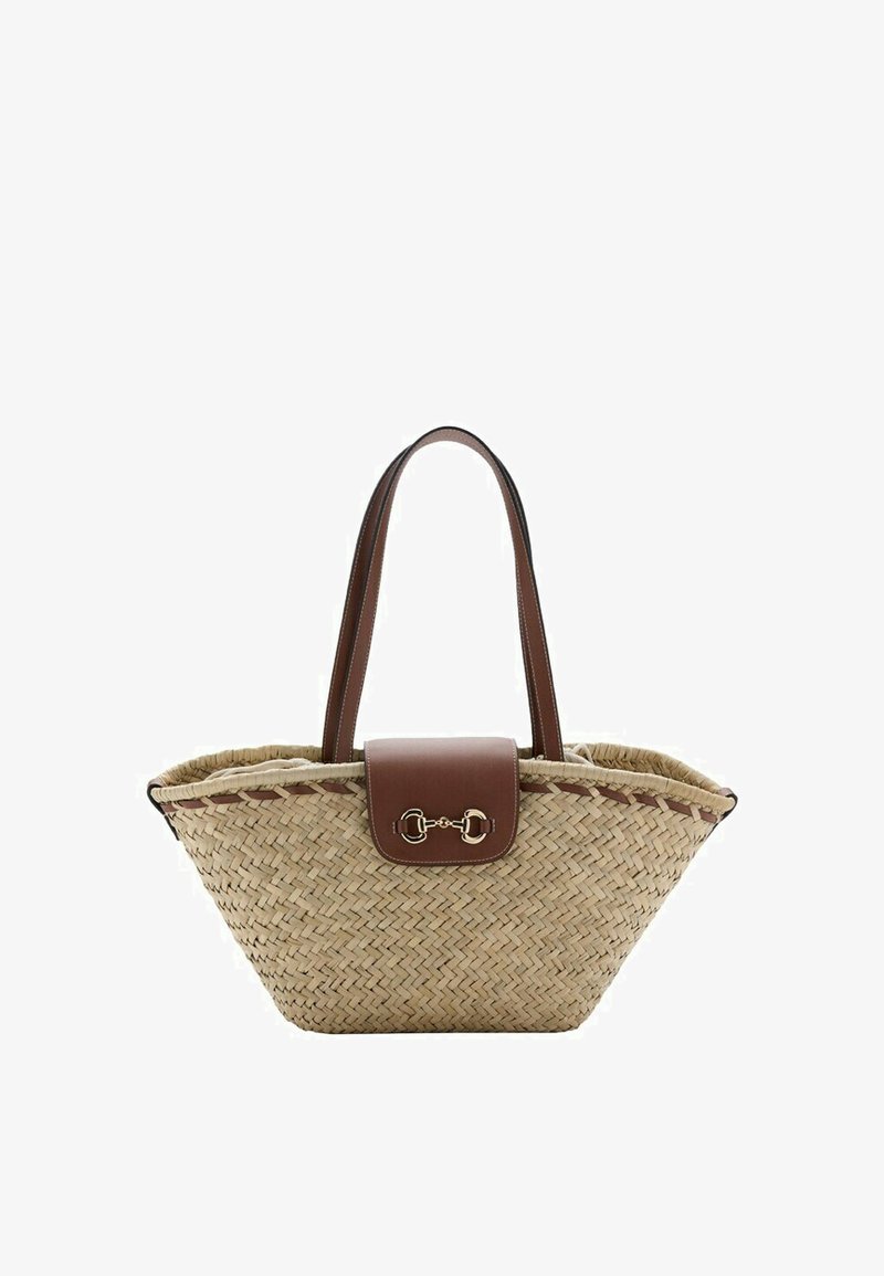 Woven straw tote bag with brown leather handles and front flap featuring a gold horsebit detail, open-top design.