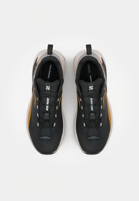 Des chaussures de sport noires et orange qui présentent une tige en synthétique, une semelle beige épaisse, un design à lacets et des accents de logo sur les côtés et la languette.