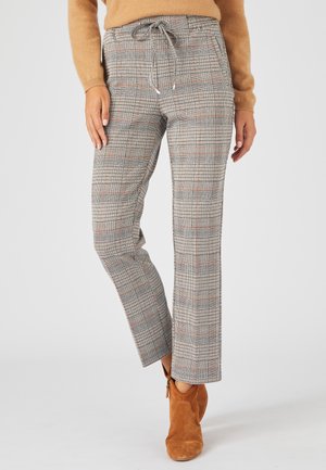 Pantalons à carreaux gris avec taille à cordon, présentant des accents rouges et un design à jambe droite. Associés à des bottines beige.