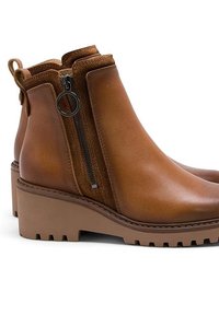 Botines de cuero marrón con cremalleras laterales, suela gruesa y perfilado liso. Cuenta con una lengüeta en la parte trasera para ponérselos con facilidad.