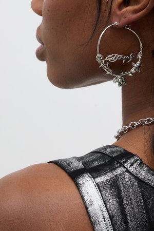 Silver hoop earrings with floral accents and the word "Crazy" integrated into the design, worn alongside a dark, textured top.