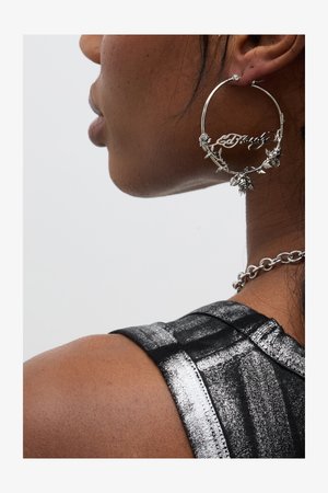 Silver hoop earrings with floral accents and the word "Crazy" integrated into the design, worn alongside a dark, textured top.