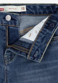 Levi's 511 Slim jeans in dark blue denim, featuring a zipper fly, single button closure, and orange stitching details. Tag visible shows size 12.
