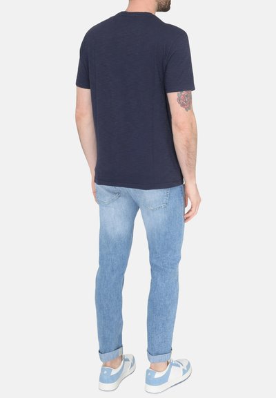T-shirt blu navy a maniche corte con scollo rotondo, abbinato a jeans azzurri e sneakers bianche con dettagli blu.