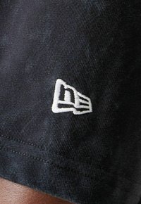 Schwarze Stoffshorts mit texturiertem Finish und einem auffälligen weißen gestickten Logo an der unteren Seite des Beins.