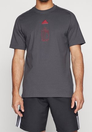 Homme portant un t-shirt Adidas gris foncé avec logo rouge et blason, assorti à un short Adidas noir avec des bandes blanches sur les côtés.