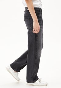 Donkergrijze denim jeans met een recht gesneden pijp, vijf zakken en stikseldetails. G gedragen met witte boottijd.