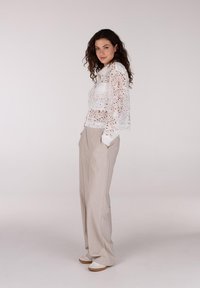 Witte kantblouse met bloemenpatroon, gecombineerd met beige wijde broek en witte sneakers. Minimalistisch ontwerp en lichte stof.