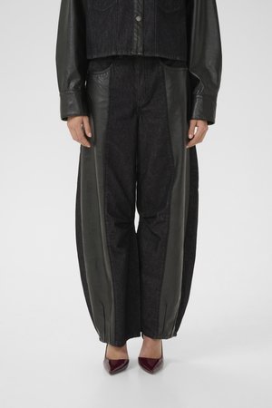 Denim trousers with black leather side panels, loose fit, and elastic cuffs at the ankles. Worn with burgundy pointed-toe heels.