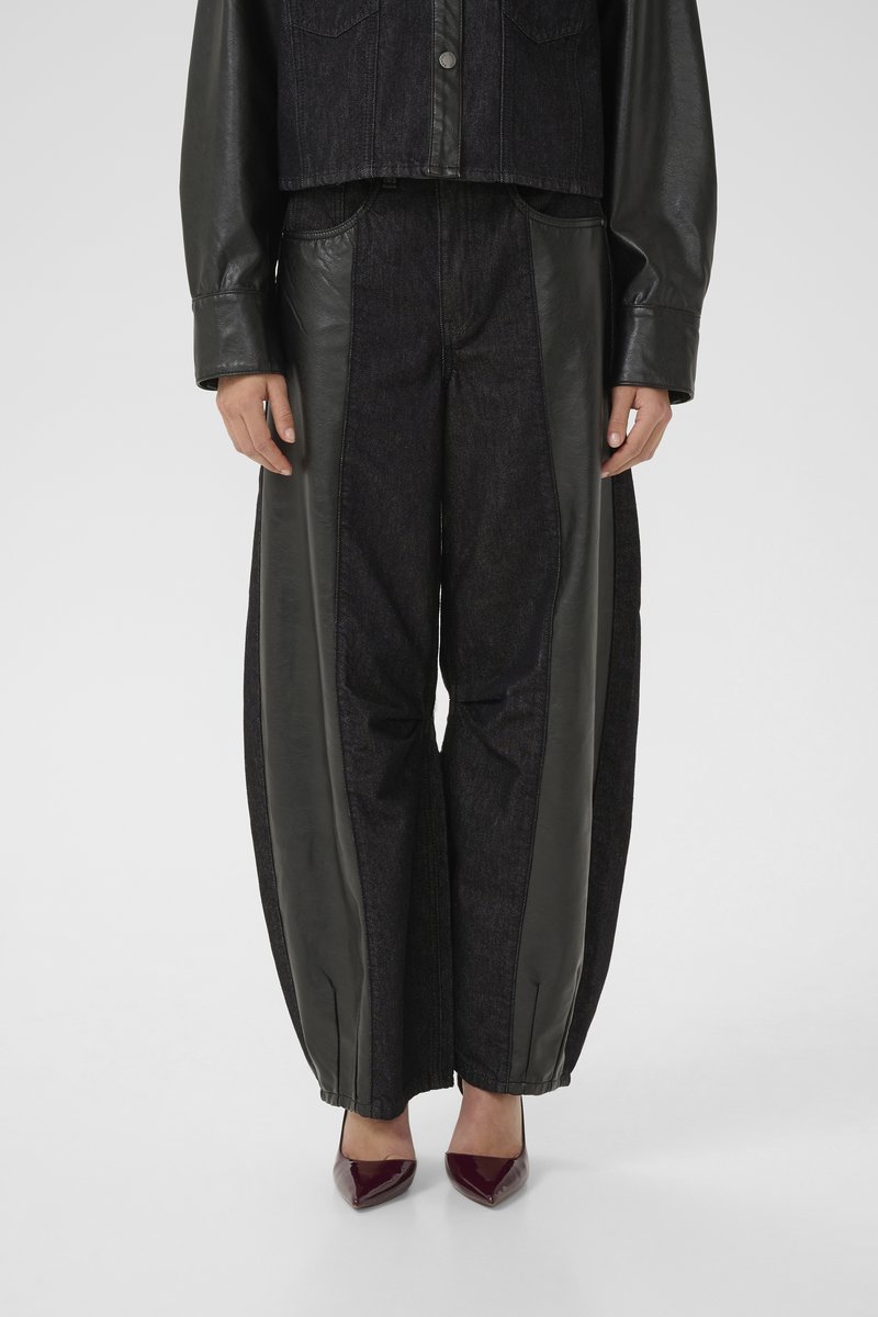 Denim trousers with black leather side panels, loose fit, and elastic cuffs at the ankles. Worn with burgundy pointed-toe heels.