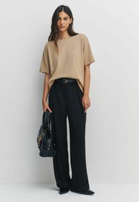 Beżowy, oversize T-shirt z krótkim rękawem, zestawiony z czarnymi spodniami o szerokiej nogawce, czarnym paskiem i teksturowaną czarną torebką.