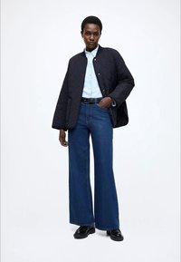 Juoda siuvinėta bombonešio striukė dėvima ant šviesiai mėlynos marškinių, derinama su plačiomis mėlynomis džinsais ir juodais batais. Lygūs tekstūros ir švarios linijos.