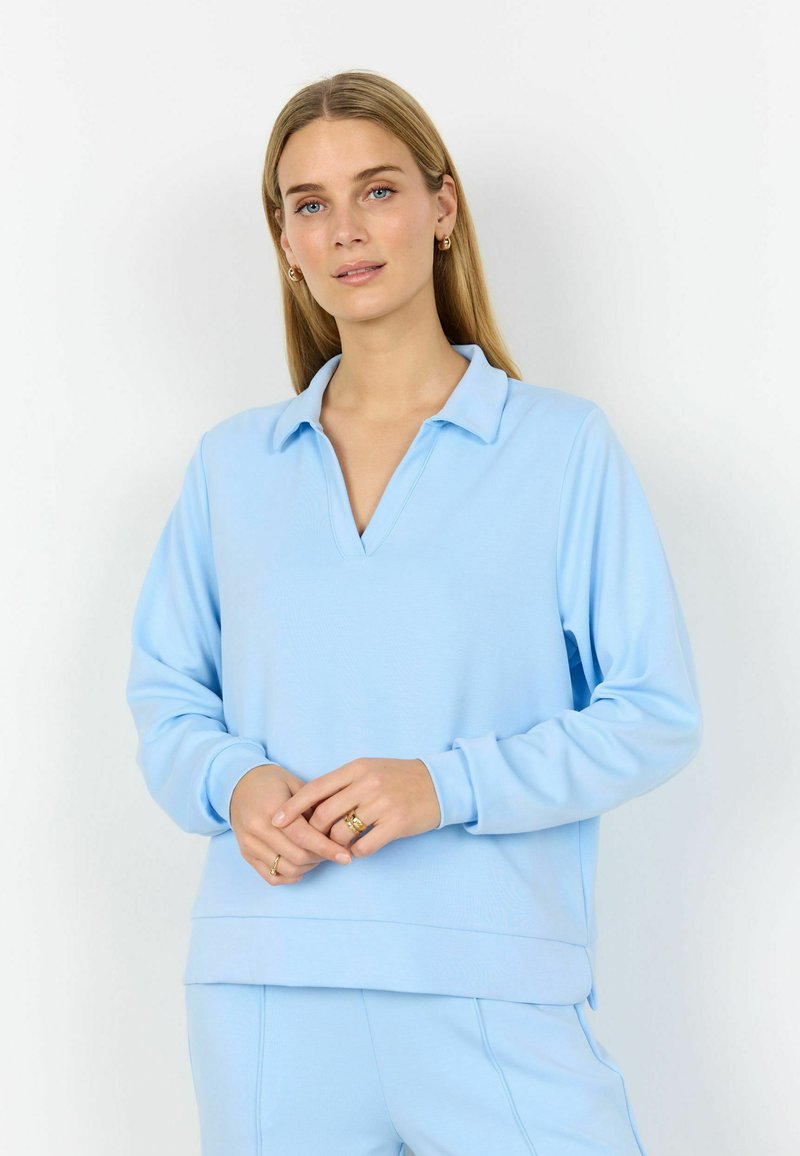 Jersey azul claro con escote en V y cuello, mangas largas y textura suave. Diseño hasta la cintura con ajuste relajado y dobladillo acanalado.