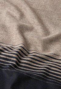 Tessuto a motivi a spina di pesce in beige e marrone, con righe blu navy nella parte inferiore. Texture morbida con pieghe e grinze visibili.