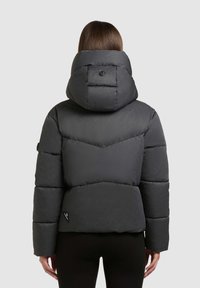 Sort pufferjakke med høj krave og aftagelig hætte. Har quiltet mønster og et lille logomærke nær kanten. Glat tekstur.