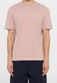 Lichtroze katoenen T-shirt met een ronde hals, korte mouwen en een klein textuurpatch op de linkerborst. Zichtbare stiksel-details.