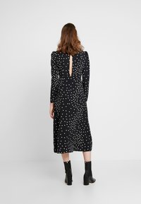 Svart klänning med prickar som har långa ärmar, ett nyckelhål på baksidan och en midilängd svängig kjol. Stylad med svarta klackstövlar.