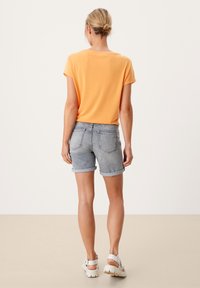 Maglietta arancione a maniche corte, abbinata a pantaloni corto in denim grigio chiaro, con orlo arrotolato. Calzature casual con suole bianche spesse.