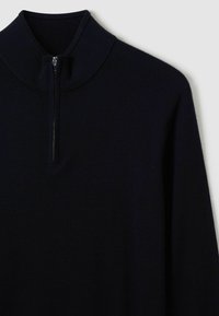 Pull en maille noir avec un col montant et une fermeture éclair à l'avant. Présente une texture lisse et des manches longues ajustées.