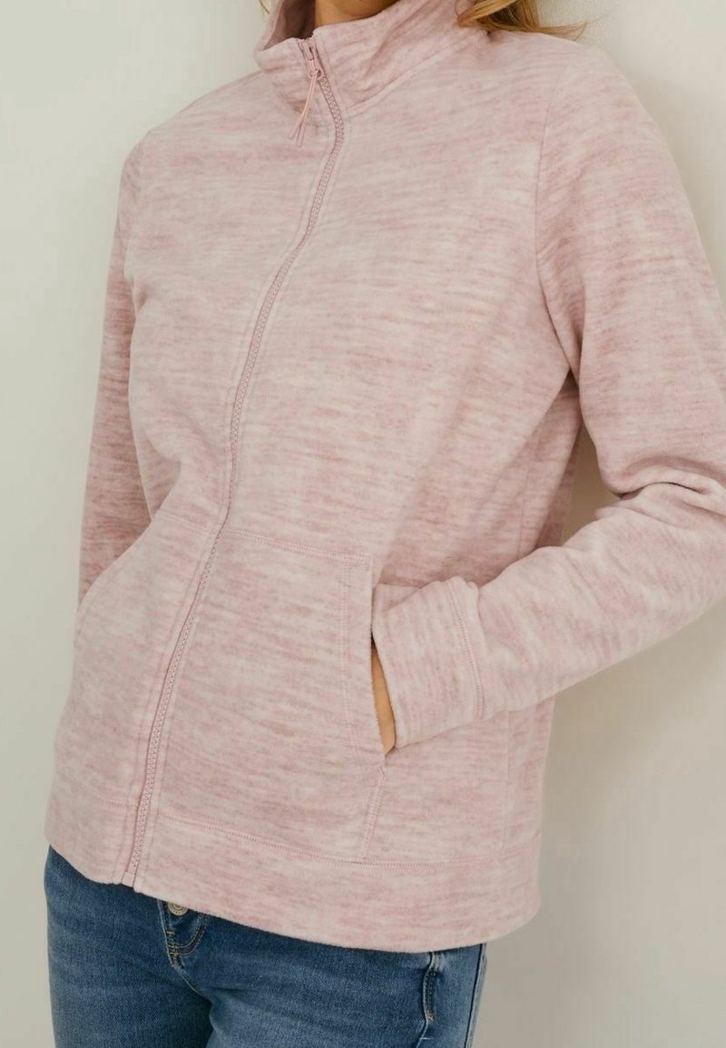 Lichtroze fleece jasje met rits en hoge kraag, textuurstof, zijzakken en contrasterende stiksels.