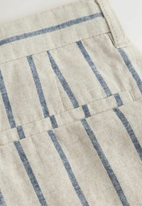 Beige linen fabric with vertical navy blue stripes and stitched seams, showing part of a pocket and waistband detail.