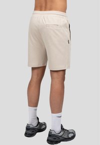 Bermudas de algodón beige con cinturilla elástica, bolsillos laterales y un bolsillo trasero, combinadas con zapatillas deportivas grises y calcetines blancos.