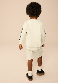 Sudadera beige clara y pantalones cortos a juego de tela suave, con un patrón de cuadros azul marino en las mangas y zapatillas casuales negras.