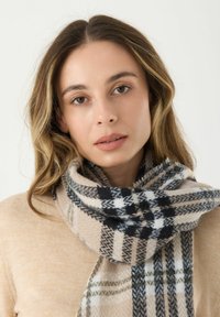 Beige en zwart geruite sjaal gemaakt van zachte stof, met een gelaagd ruitpatroon. Gestructureerde afwerking met franjeranden.