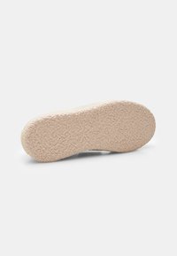 Suola di scarpa in gomma, colore beige chiaro, superficie texture con un aspetto morbido e lanoso, forma arrotondata con una leggera curvatura nel tallone.