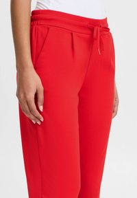 Rode joggingbroek met een elastische tailleband, trekkoordsluiting, zijzakken en een zachte textuur. Kenmerkt zich door subtiele plooien aan de voorkant.