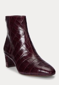 Bottine en cuir bordeaux avec un bout pointu, texture crocodile et un talon bloc de hauteur intermédiaire. Fermeture éclair à l'arrière.