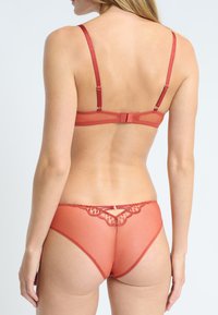 Czerwona bielizna z koronkowym wykończeniem, zawierająca biustonosz z siateczki z regulowanymi ramiączkami oraz dopasowany stringi z ozdobnymi detalami z tyłu.