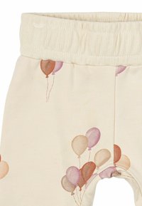 Krämfärgade leggins med en mjuk textur som har ett mönster av ballonger i nyanser av rosa, brunt och lila på det ena benet.